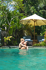 Image showing Happy couple kissing while relaxing in outdoor spa infinity swimming pool surrounded with lush tropical greenery of Ubud, Bali. Luxury spa and wellness vacation retreat concept