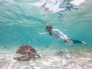 Image showing Woman on vacations wearing snokeling mask swimming with sea turtle in turquoise blue water of Gili islands, Indonesia. Underwater photo.