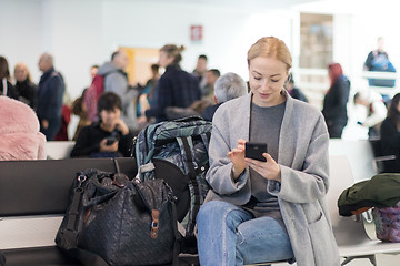 Image showing Female traveler using her cell phone while waiting to board a plane at departure gates at airport terminal.