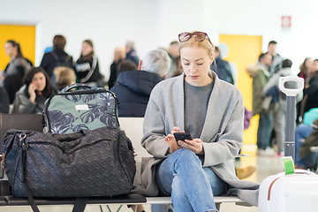 Image showing Female traveler reading on her cell phone while waiting to board a plane at departure gates at airport terminal.