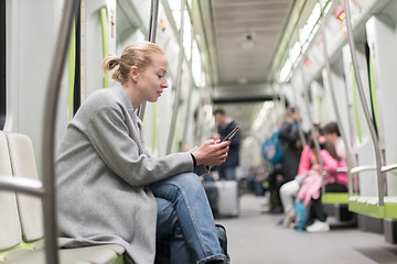 Image showing Beautiful blonde woman wearing winter coat reading on the phone while traveling by metro public transport.