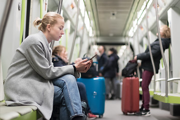 Image showing Beautiful blonde woman wearing winter coat reading on the phone while traveling by metro public transport.