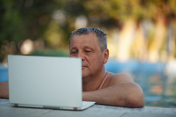 Image showing A middle aged man in the swimming pool watching something on a laptop