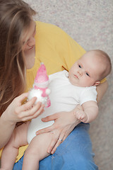 Image showing A baby boy in arms of a long haired woman looking at a toy in her hand