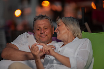 Image showing Cheerful mature couple relaxing outdoor and looking through the mobile photos