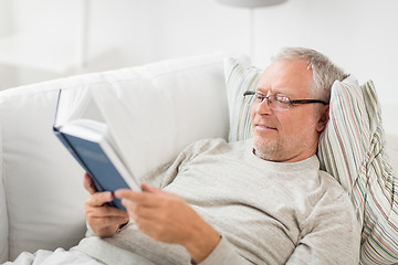 Image showing senior man lying on sofa and reading book at home