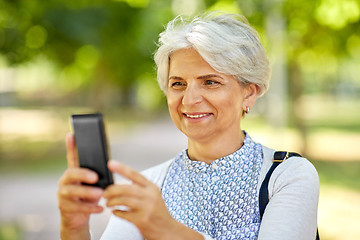 Image showing senior woman photographing by cell at summer park