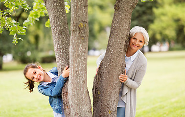 Image showing grandmother and granddaughter behind tree at park