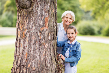 Image showing grandmother and granddaughter behind tree at park