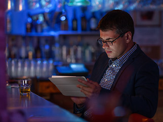 Image showing Businessman with tablet pc and whisky at the bar counter