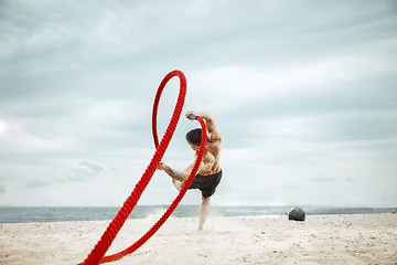 Image showing Young healthy man athlete doing squats at the beach