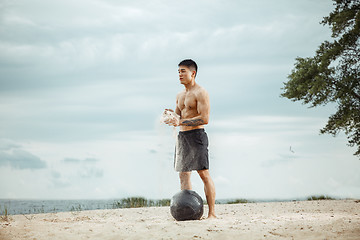 Image showing Young healthy man athlete doing squats at the beach