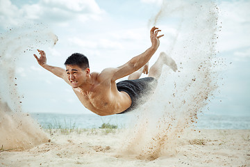 Image showing Young healthy man athlete doing squats at the beach