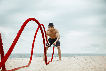 Image showing Young healthy man athlete doing squats at the beach