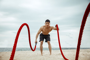 Image showing Young healthy man athlete doing squats at the beach