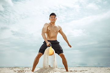 Image showing Young healthy man athlete doing squats at the beach