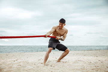 Image showing Young healthy man athlete doing squats at the beach