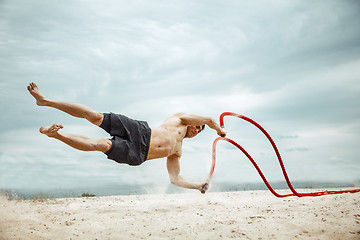 Image showing Young healthy man athlete doing squats at the beach