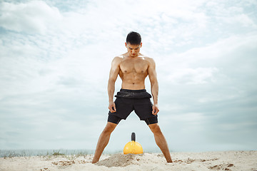 Image showing Young healthy man athlete doing squats at the beach