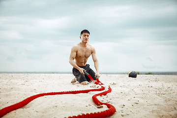 Image showing Young healthy man athlete doing squats at the beach