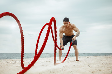 Image showing Young healthy man athlete doing squats at the beach