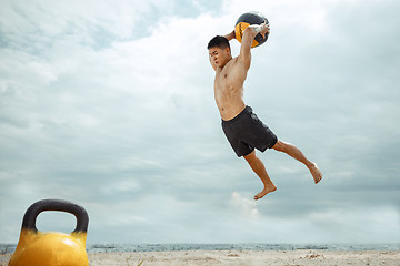 Image showing Young healthy man athlete doing squats at the beach