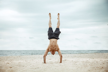 Image showing Young healthy man athlete doing squats at the beach