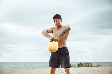 Image showing Young healthy man athlete doing squats at the beach