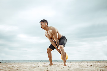 Image showing Young healthy man athlete doing squats at the beach