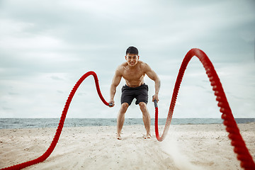 Image showing Young healthy man athlete doing squats at the beach