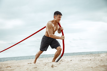 Image showing Young healthy man athlete doing squats at the beach