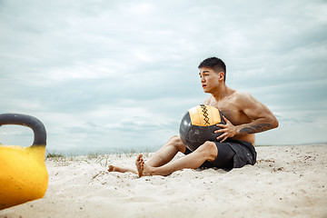 Image showing Young healthy man athlete doing squats at the beach