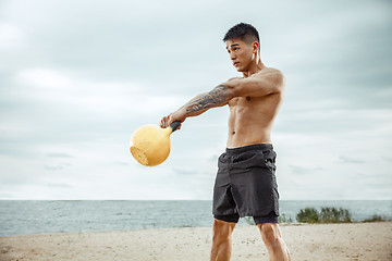 Image showing Young healthy man athlete doing squats at the beach