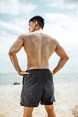 Image showing Young healthy man athlete doing squats at the beach