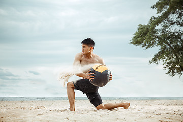 Image showing Young healthy man athlete doing squats at the beach