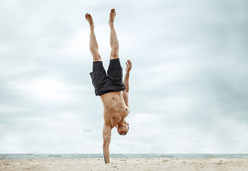 Image showing Young healthy man athlete doing squats at the beach