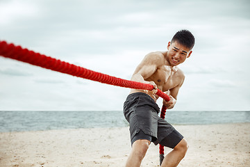 Image showing Young healthy man athlete doing squats at the beach