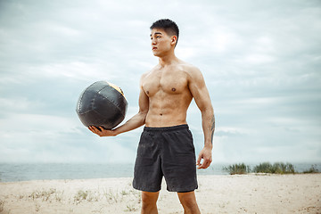 Image showing Young healthy man athlete doing squats at the beach