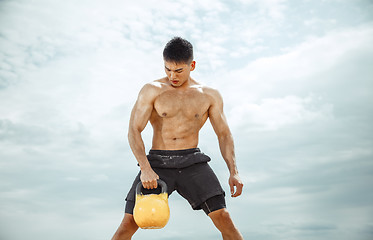 Image showing Young healthy man athlete doing squats at the beach