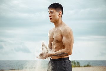 Image showing Young healthy man athlete doing squats at the beach