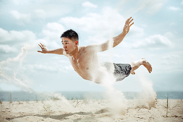 Image showing Young healthy man athlete doing squats at the beach