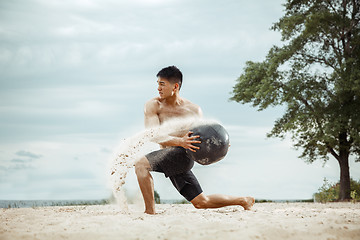 Image showing Young healthy man athlete doing squats at the beach