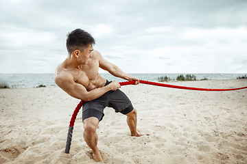 Image showing Young healthy man athlete doing squats at the beach