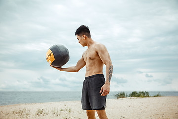 Image showing Young healthy man athlete doing squats at the beach