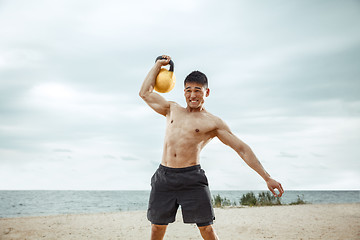 Image showing Young healthy man athlete doing squats at the beach