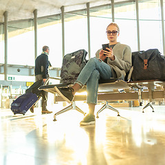 Image showing Female traveler using her cell phone while waiting to board a plane at departure gates at airport terminal.