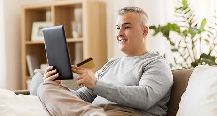 Image showing man with tablet pc and credit card on sofa at home