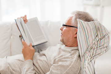 Image showing senior man lying on sofa and reading book at home