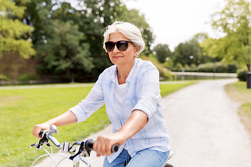 Image showing happy senior woman riding bicycle at summer park