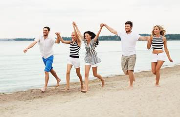 Image showing friends in striped clothes running along beach